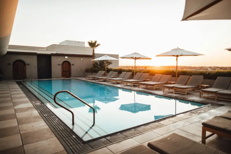 Backyard pool at sunset with a travertine deck and a modern Dallas home behind it